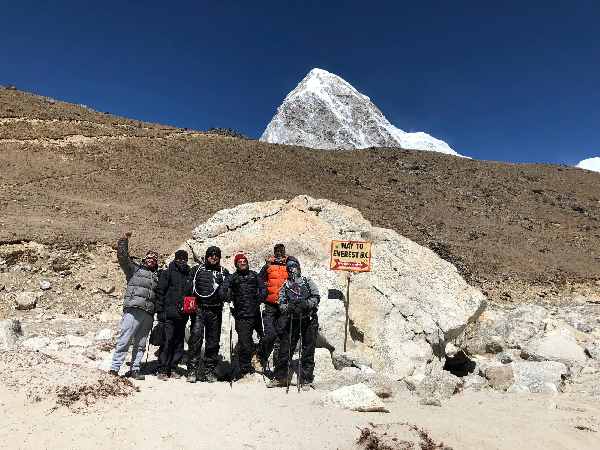 Climbers at the Everest Base Camp sign with a snow-capped peak behind